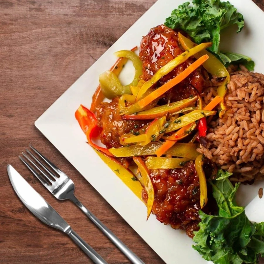 Square plate with rice, meat in sauce and vegetables on wooden table and cutlery on the side